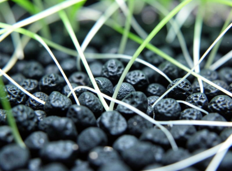 Dark active aqua soil granules in a planted aquarium with green plant roots growing through them