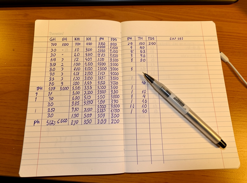 Handwritten aquarium parameter logbook with GH KH TDS columns and a TDS pen on the page