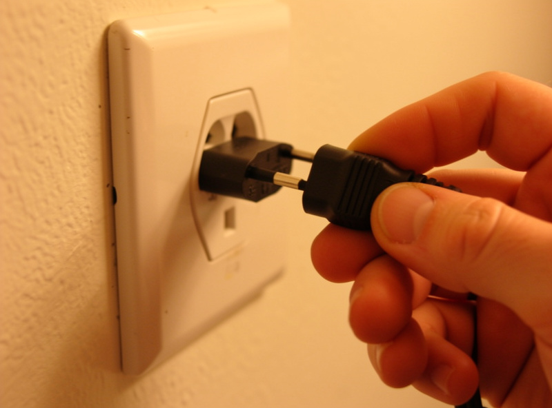 Fingers checking the contacts of an LED power adapter plug pulled from a wall outlet