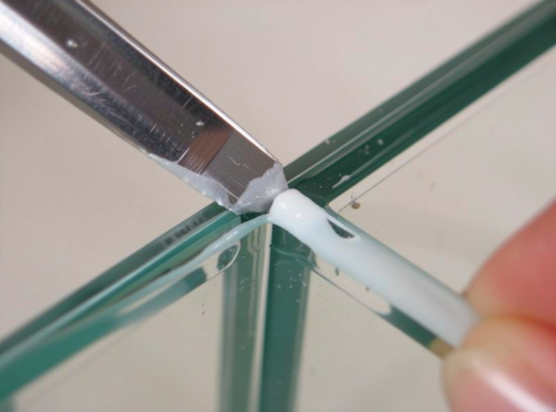 Razor blade scraping old cured silicone out of the inside corner seam of an empty glass aquarium